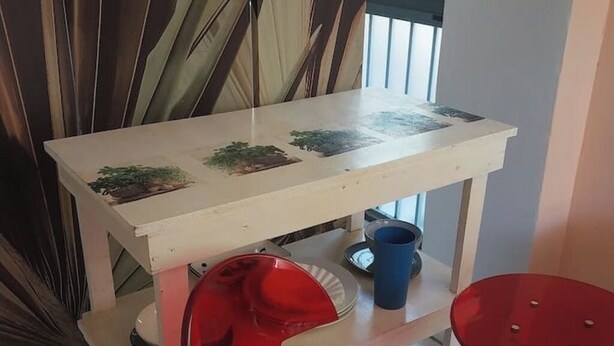 Una mesa blanca con una superficie decorativa, una silla roja y una taza azul sobre un estante.