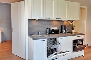 Eine kompakte Küche mit weißen Schränken, einem integrierten Geschirrspüler, einer Kaffeemaschine und einem kleinen Backofen.