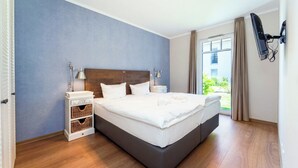 Ein Hotelzimmer mit einem großen Bett, Nachttischen, einem an der Wand montierten Fernseher und einem Fenster mit Vorhängen.