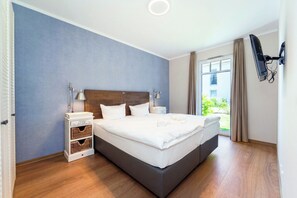 Ett hotellrum med en stor säng, sängbord, en tv som är monterad på väggen och ett fönster med gardiner.