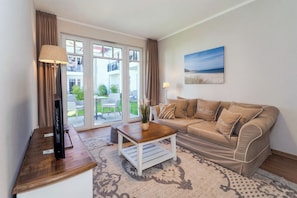 A living room with a sofa, a coffee table, a TV on a stand, and a view of a balcony with outdoor furniture. - Baltischer Hof apartment 10 (Ostseebad Boltenhagen)