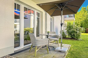 Une terrasse extérieure avec des chaises en osier, une table et un grand parasol.