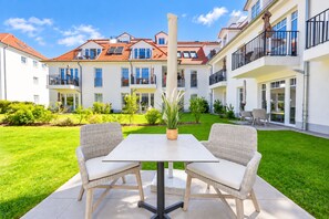 Une cour avec une table et des chaises, entourée de verdure et bordée d’un immeuble doté de balcons.