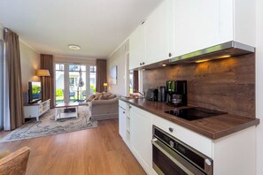 A modern kitchen with a built-in stove, a coffee maker, and a dining area with a sofa and table. - Baltischer Hof Apartment 09 (Ostseebad Boltenhagen)