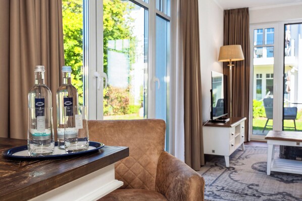 Ein Zimmer mit einem großen Fenster, einem braunen Ledersofa, einem Holztisch mit zwei Flaschen, einer Lampe und einem Fernseher.