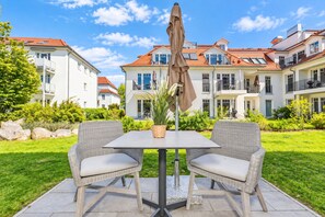 A patio with two wicker chairs and a table, a brown umbrella, and a potted plant. - Baltischer Hof Apartment 09 (Ostseebad Boltenhagen)
