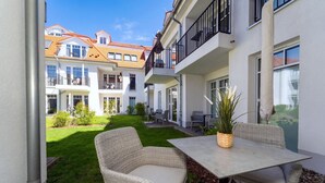 Ein Innenhof mit Tisch und Stühlen, einem Blumentopf und Blick auf ein mehrstöckiges Gebäude mit Balkonen.