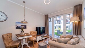 Ein modernes Wohnzimmer mit Flachbildfernseher, Esstisch, Sofa und großem Fenster mit Vorhängen.