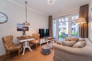 A modern living room with a flat-screen TV, a dining table, a sofa, and a large window with curtains. - Baltischer Hof apartment 11 (Ostseebad Boltenhagen)