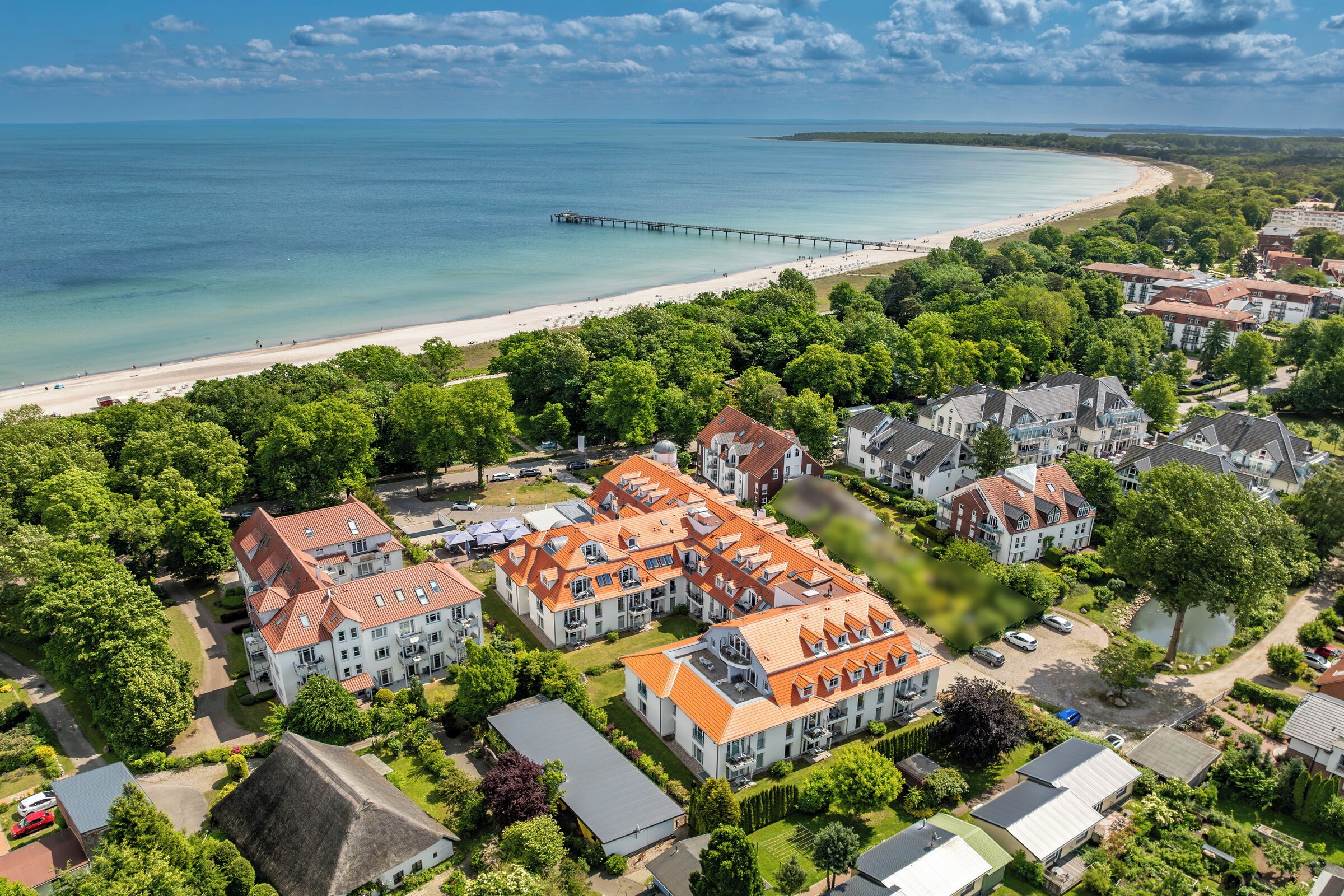 Een kustgebied met woonhuizen, een strand, een pier en huizen met rode dakpannen.