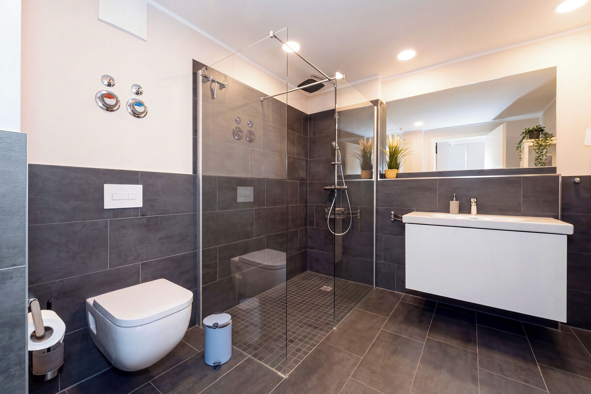 Een moderne badkamer met een douchecabine van glas, een wit toilet en een witte wastafel met een spiegel erboven.