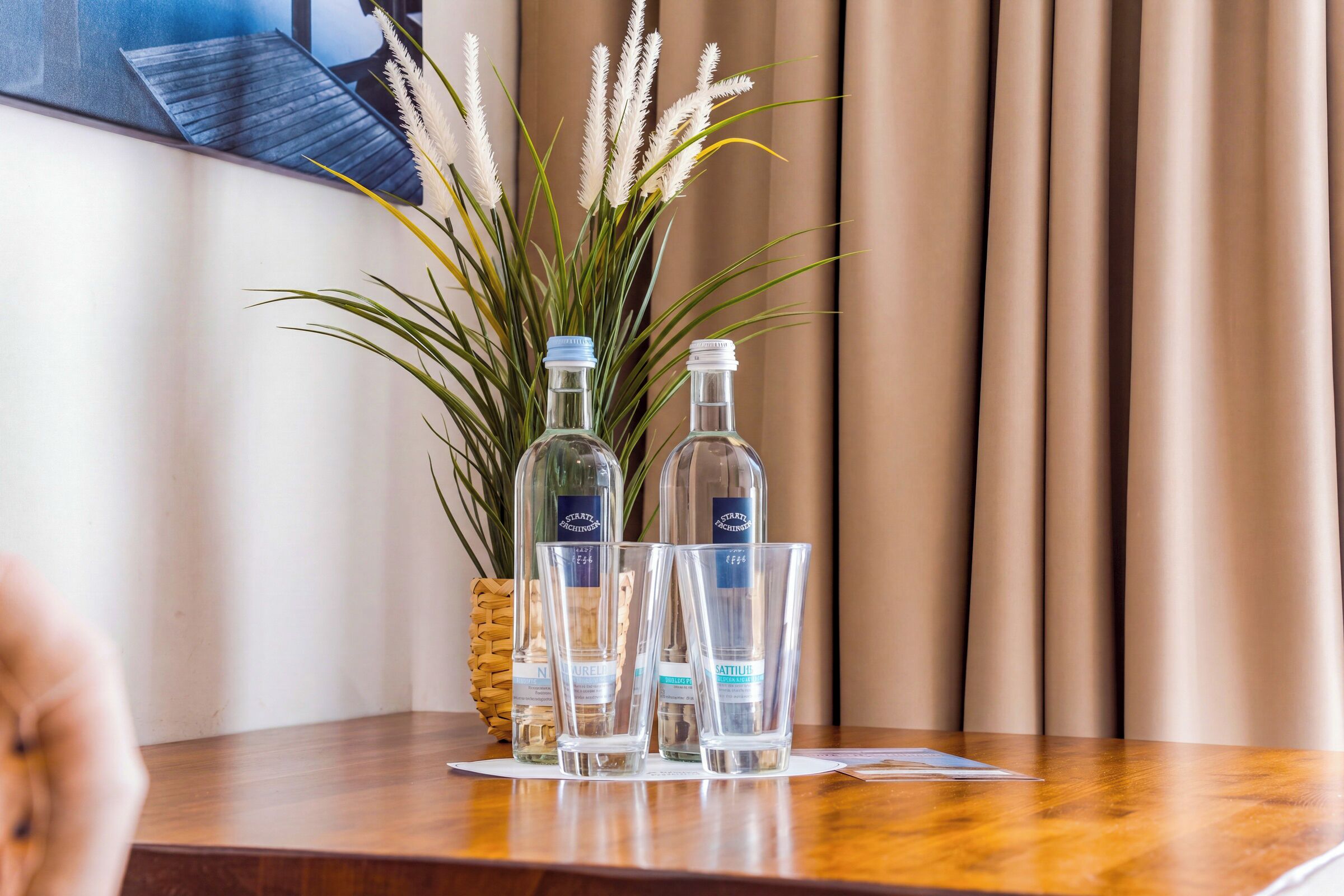 Een tafel met twee flessen, twee glaasjes en een plant met witte bloemen, allemaal op een houten oppervlak.