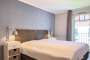 Ein Schlafzimmer mit einem großen Bett, zwei Nachttischen inklusive Lampen, einem Kopfteil und einem Fenster mit Vorhängen.