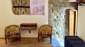 A room with a stone wall, two antique upholstered chairs, a small wooden table, and a large abstract painting. - DUOMO, your private garden in TORRE: THE SFINGE OF THE SECRET GARDEN. (Firenze)