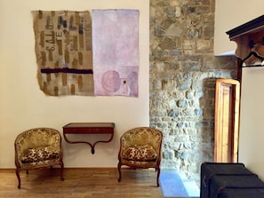 Ein Zimmer mit einer Steinswand, zwei antiken Polsterstühlen, einem kleinen Holztisch und einem großen abstrakten Gemälde.