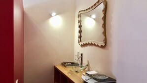 A bathroom with a wooden vanity, a glass bowl sink, a mirror with a decorative frame, and two wall-mounted lights. - DUOMO, your private garden in TORRE: THE SFINGE OF THE SECRET GARDEN. (Firenze)