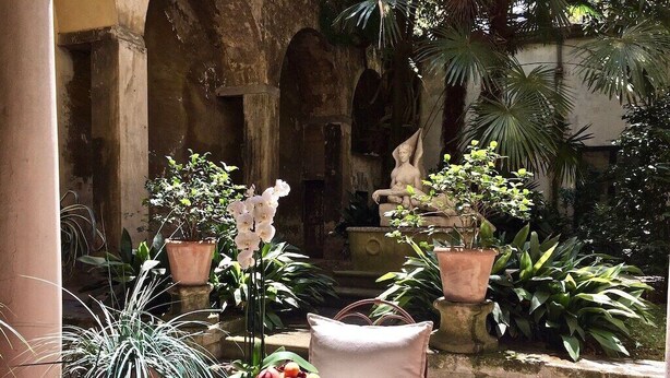 A table set with breakfast items in an outdoor courtyard with potted plants and a statue. - DUOMO, your private garden in TORRE: THE SFINGE OF THE SECRET GARDEN. (Firenze)
