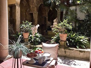A table set with breakfast items in an outdoor courtyard with potted plants and a statue. - DUOMO, Your Private Garden in TORRE: THE SPHINX OF THE SECRET GARDEN. (Firenze)