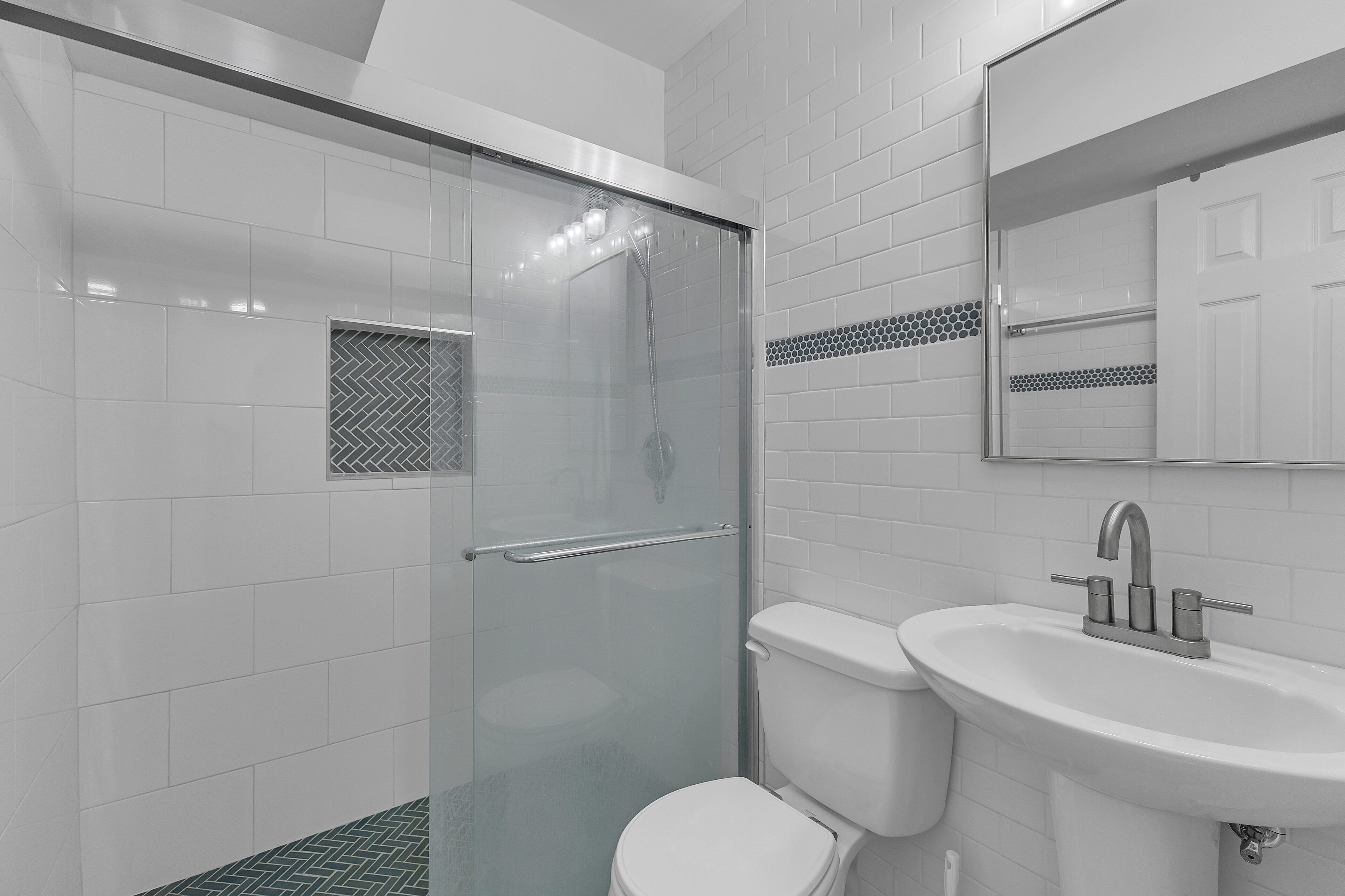 A modern bathroom with a glass-enclosed shower, a white toilet, and a sink with a mirror above it.