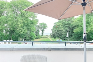 Ein Sitzbereich im Freien mit Blick auf einen Park und ein Gewässer.