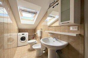 Un baño moderno con tragaluz, lavadora, inodoro y lavamanos.