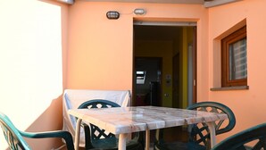 Un balcón con una mesa y sillas, una puerta que da al interior y un ventanal con marco de madera.