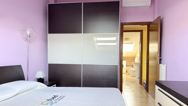 Habitación de hotel con cama, mesita de noche, lámpara, armario y baño visible a través de una puerta abierta.