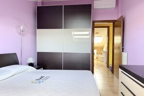 Habitación de hotel con cama, mesita de noche, lámpara, armario y baño visible a través de una puerta abierta.