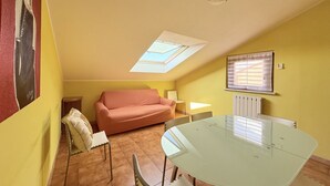 Una habitación con una mesa de vidrio, un sofá, una silla, un radiador y un tragaluz.