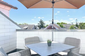 Eine Terrasse mit Tisch und Stühlen, einem Blumentopf und einem großen Sonnenschirm.
