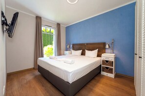 A hotel room with a large bed, a nightstand, a lamp, and a view of greenery outside. - Baltischer Hof Apartment 05 (Ostseebad Boltenhagen)