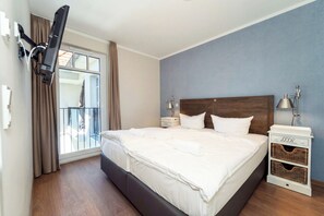 Ein Hotelzimmer mit einem großen Bett, einem Nachttisch mit Lampe, einem an der Wand montierten Fernseher und einem Fenster mit Vorhängen.