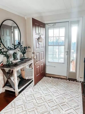 Un couloir avec un banc en bois, un miroir et un tapis blanc.
