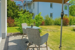 En udendørs patio med et bord og stole, en pergola og udsigt til en boligbygning.