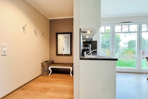 Ein modernes Interieur mit einer Holzbank, einem wandmontierten Spiegel und einer Küchenzeile mit großem Fenster.