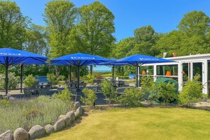 A patio area with blue umbrellas, outdoor seating, and a view of a building with orange lights. - Baltischer Hof apartment 18 (Ostseebad Boltenhagen)