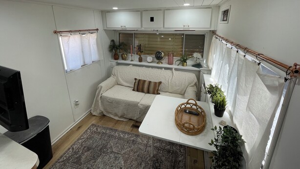 En kompakt autocamper-indretning med sofa, lille bord, TV og loftventilator.
