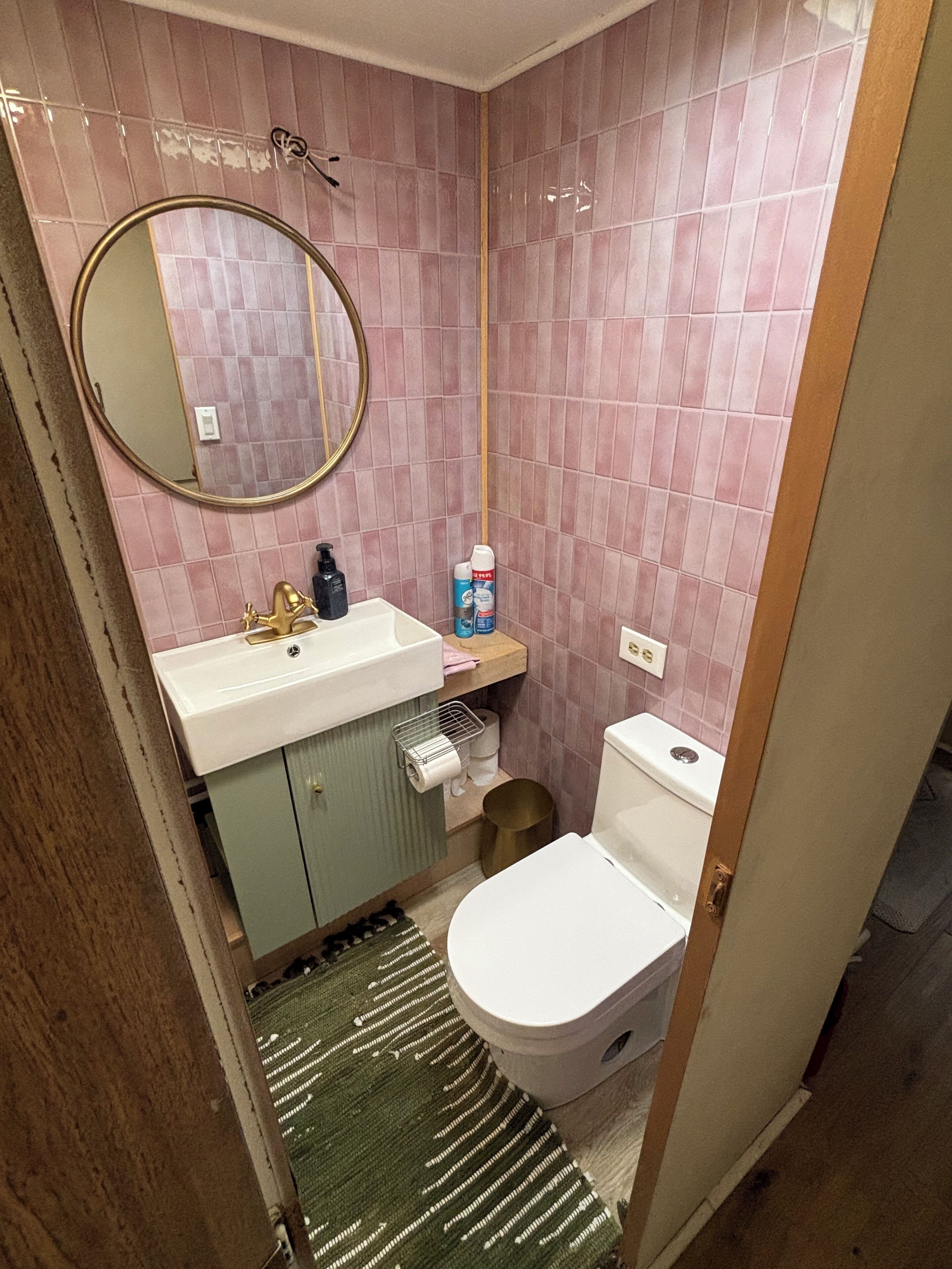 Een kleine badkamer met toilet, wastafel en spiegel. Er ligt een rol toiletpapier en staat een fles handzeep op het aanrecht.
