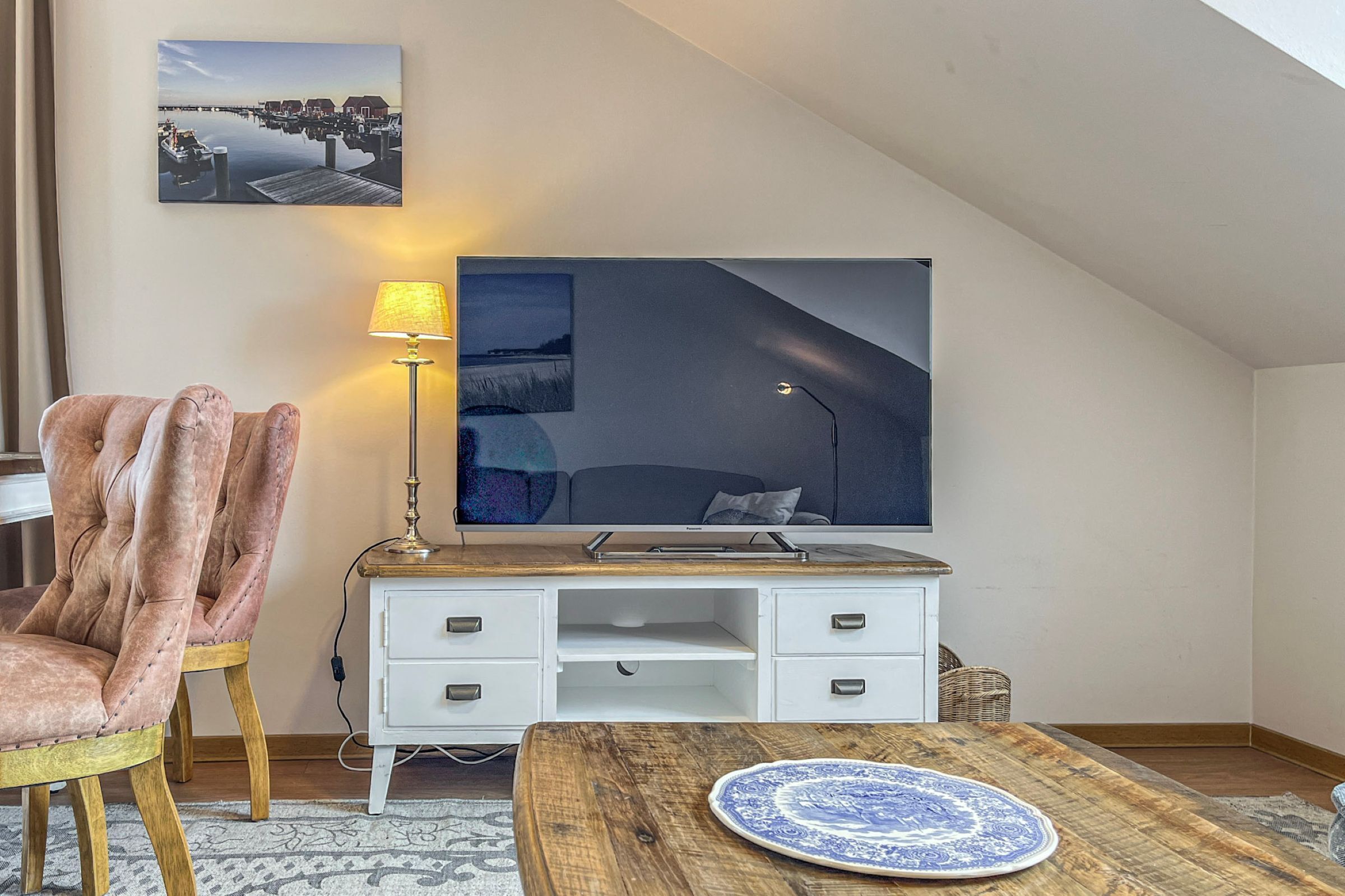 A modern room with a loft bed, a desk with a lamp, a chair, and a large painting on the wall.
