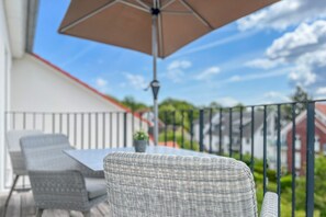 Ein Balkon mit Korbmöbeln, einem Tisch und einem Sonnenschirm.