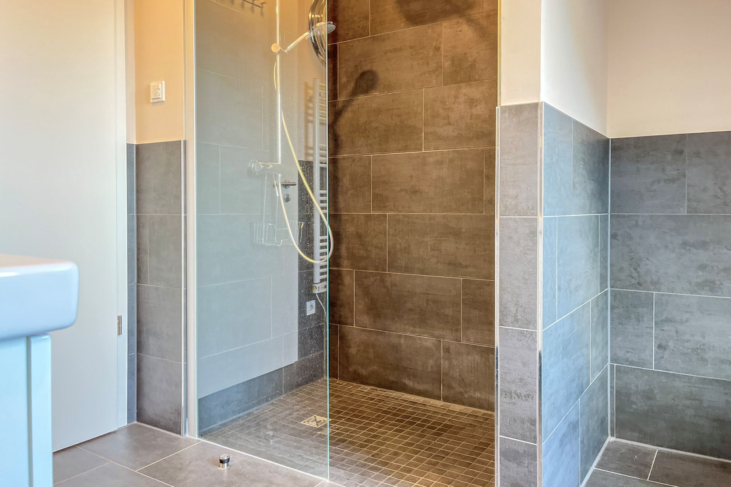 Een douche met een glazen deur, betegelde wanden en een betegelde vloer.