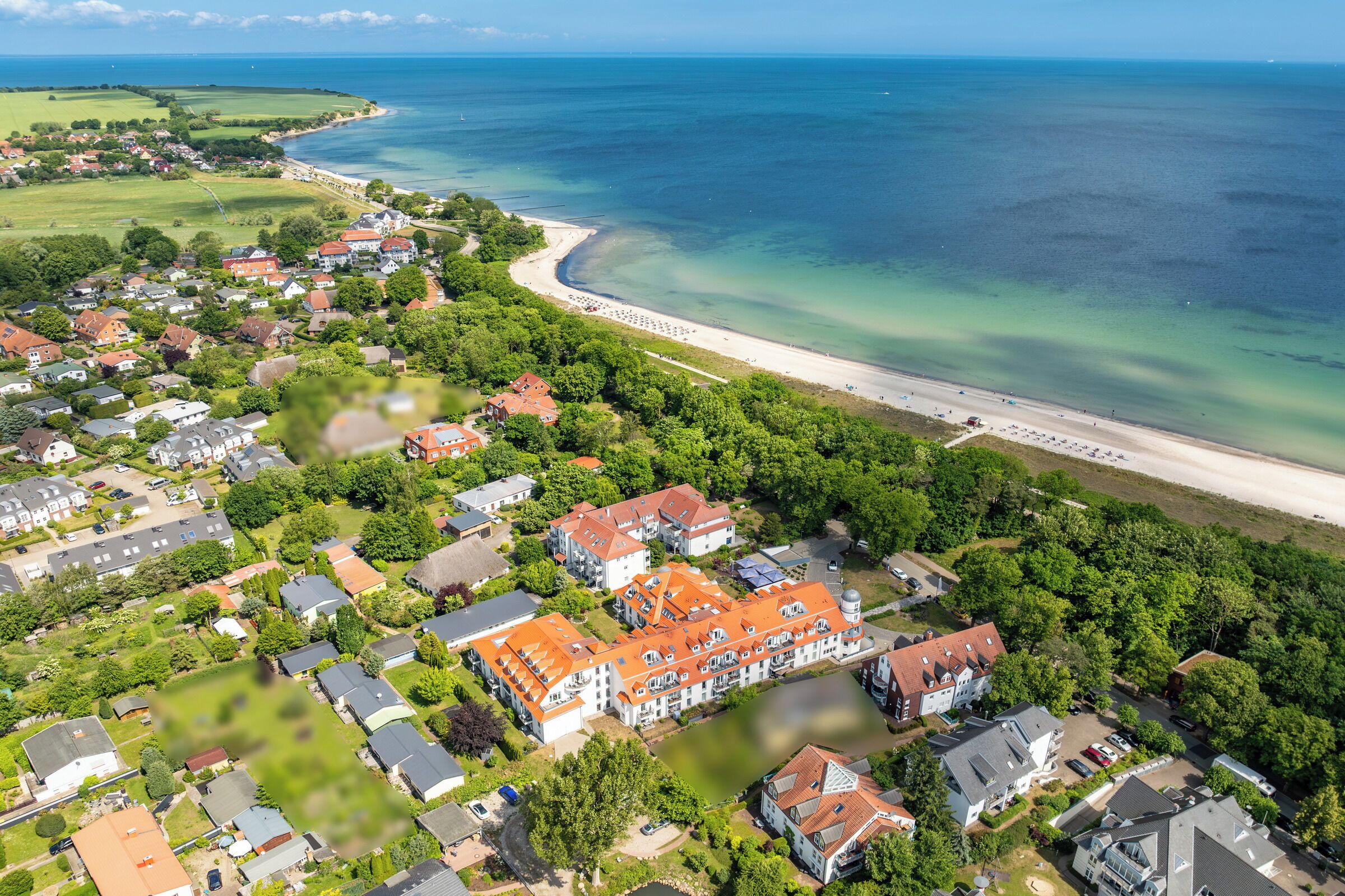 An aerial view of a coastal residential area with houses, a beach, and a large body of water.