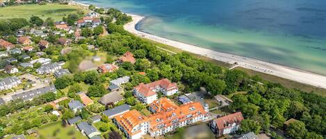 An aerial view of a coastal residential area with houses, a beach, and a large body of water.