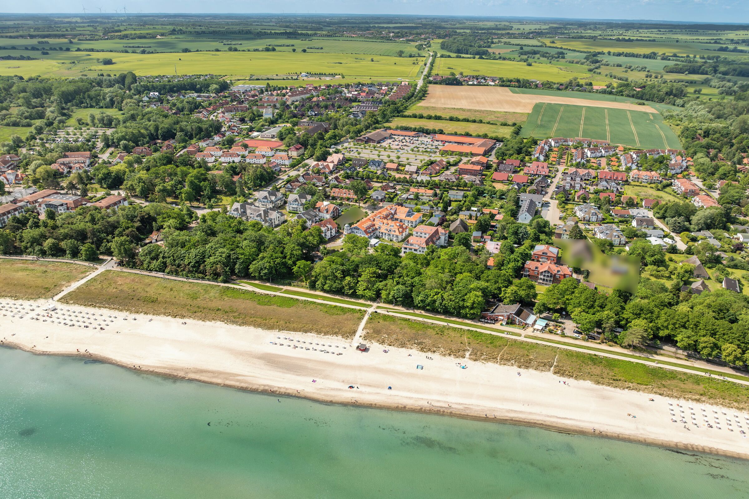 An aerial view of a coastal town with residential buildings, a beach, and green fields.