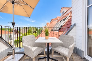 A balcony with two wicker chairs, a table, and a beige umbrella. - Baltischer Hof apartment 56 (Ostseebad Boltenhagen)