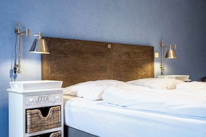 A neatly made bed with white linens, two bedside lamps, a wooden headboard, and a white nightstand with a basket. - Baltischer Hof apartment 56 (Ostseebad Boltenhagen)