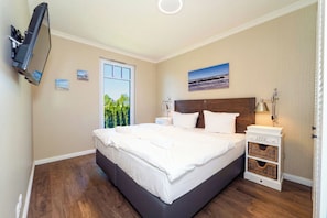 Un dormitorio con cama, mesitas de noche, televisor y ventana con vistas.