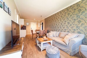 Ein Wohnzimmer mit Sofa, Hocker, Couchtisch und Essbereich mit Stühlen.