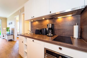 Eine moderne Küche mit weißen Schränken, einer Holzarbeitsplatte, einer Kaffeemaschine und einem Backofen.