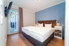 Ein Hotelzimmer mit Bett, Wandfernseher, Nachttisch und einem Fenster mit Vorhängen.